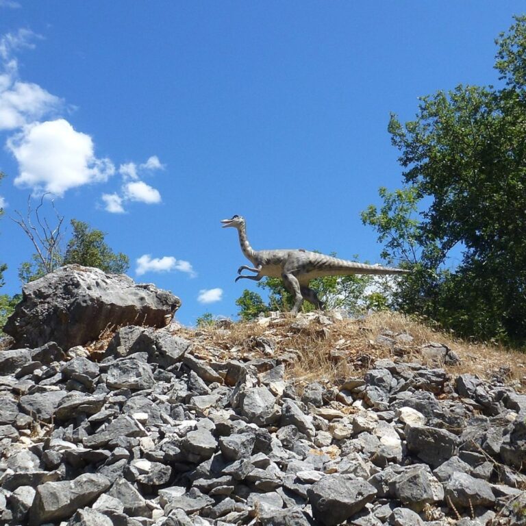 Dinosaur model standing on rocks under a blue sky at Dinopark Funtana in Istria, Croatia.